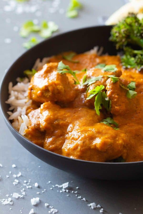 Close-up shot of texture of butter chicken in a grey bowl topped with parsley