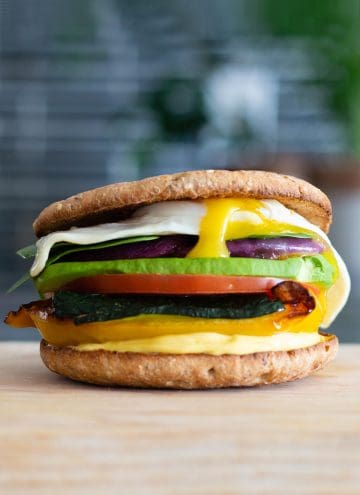 multi-layered sandwich with different colored vegetables and a fried egg on top on a cutting board