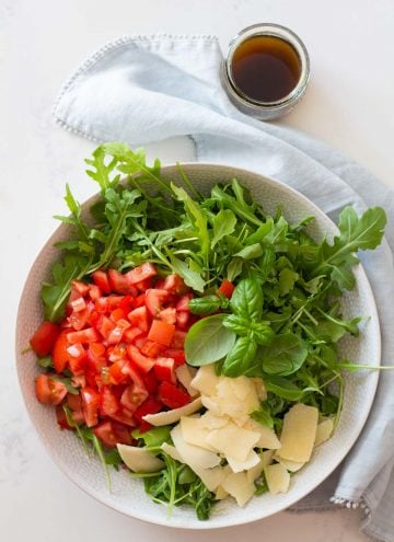arugula, diced tomato, and shaved parmesan in a white salad bowl