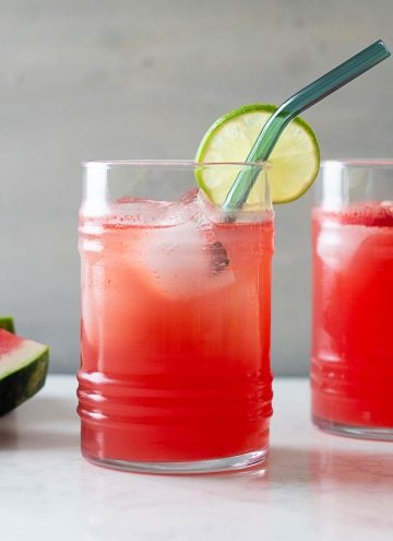 watermelon agua fresca in a glass with lime slice at edge and blue glass straw