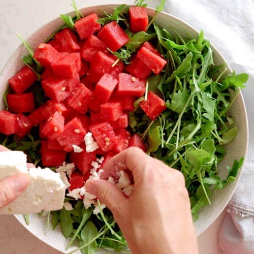 crumbleing feta cheese into salad bowl