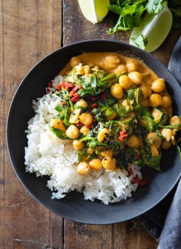 Bowl with white rice and coconut chickpea curry with baby spinach.