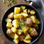 Cooked cut up red potatoes in a grey bowl garnished with fresh thyme.