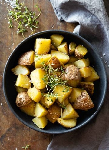 Cooked cut up red potatoes in a grey bowl garnished with fresh thyme.