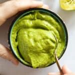 Avocado Dip in a bowl with a hand scooping out a spoon.