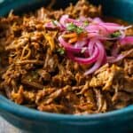 Closeup look of texture of Cochinita Pibil served in a blue bowl and topped with red onion.