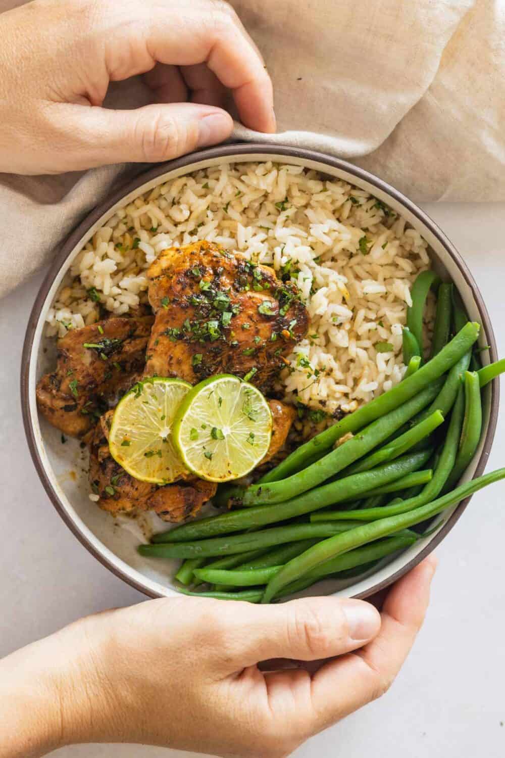 Coconut rice, cilantro lime chicken thighs, and green beans in a plate held in hands.