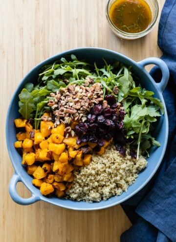 Roasted butternut squash, quinoa, chopped pecans, dried cranberries, arugula in a blue salad bowl.