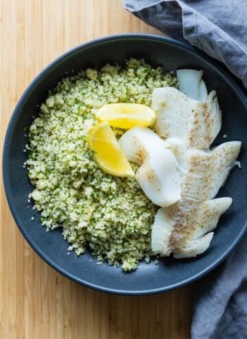 haddock on a bed of couscous with herbs and two lemon sliced on top.