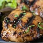 close-up image of a piece of balsamic grilled chicken thigh on a grey plate with salad in the background.