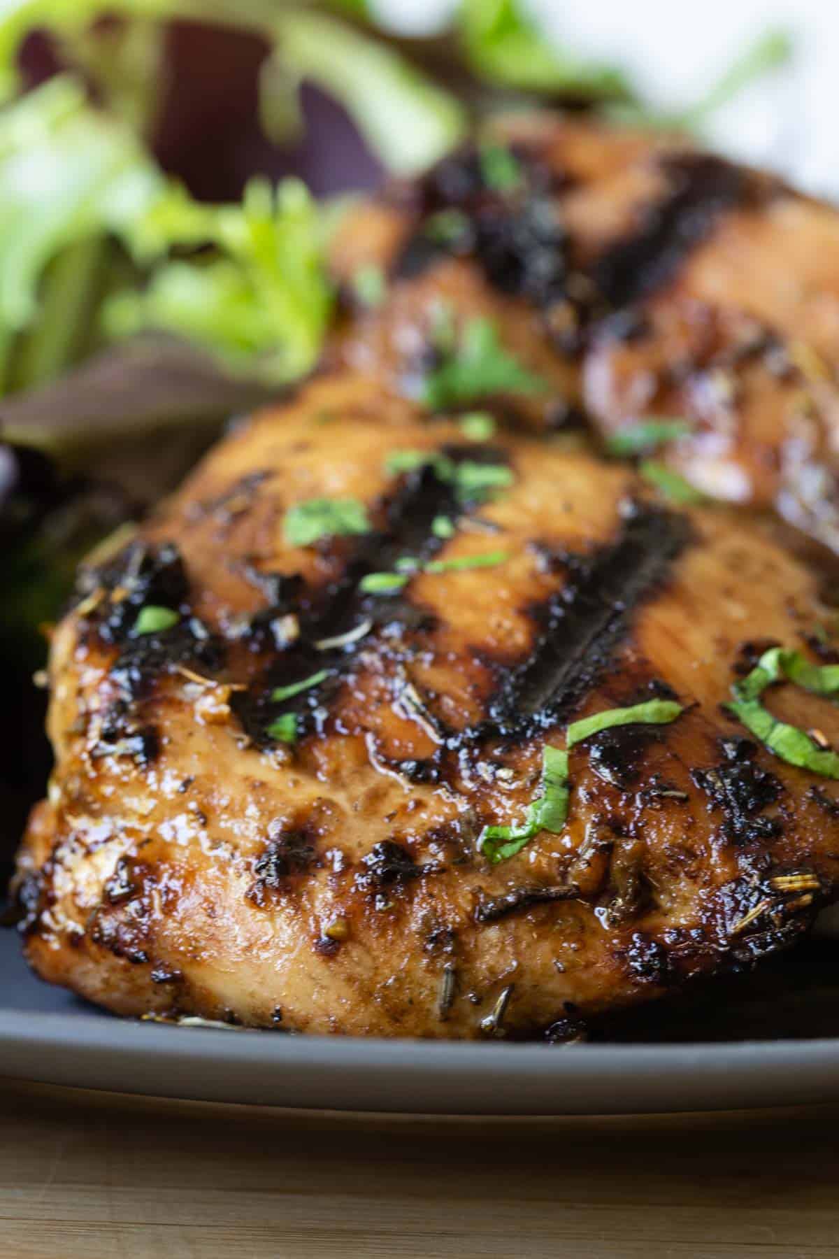 close-up image of a piece of balsamic grilled chicken thigh on a grey plate with salad in the background.