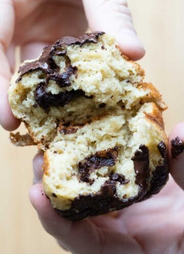 hands pulling apart a healthy banana muffin showing inside texture and dark chocolate bits.