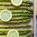 grilled asparagus on a baking sheet with lemon slices on top.