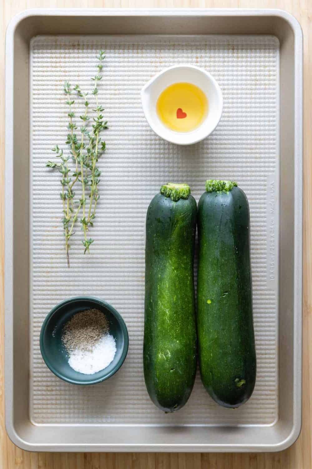 Zucchini, thyme, oil, salt and pepper laid out on a baking sheet.