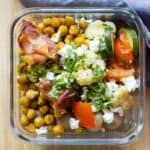 Glass meal prep container filled with chickpeas, vegetables, and prosciutto.