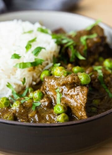 Close-up image of seco de carne in a shallow bowl with white rice in the back.