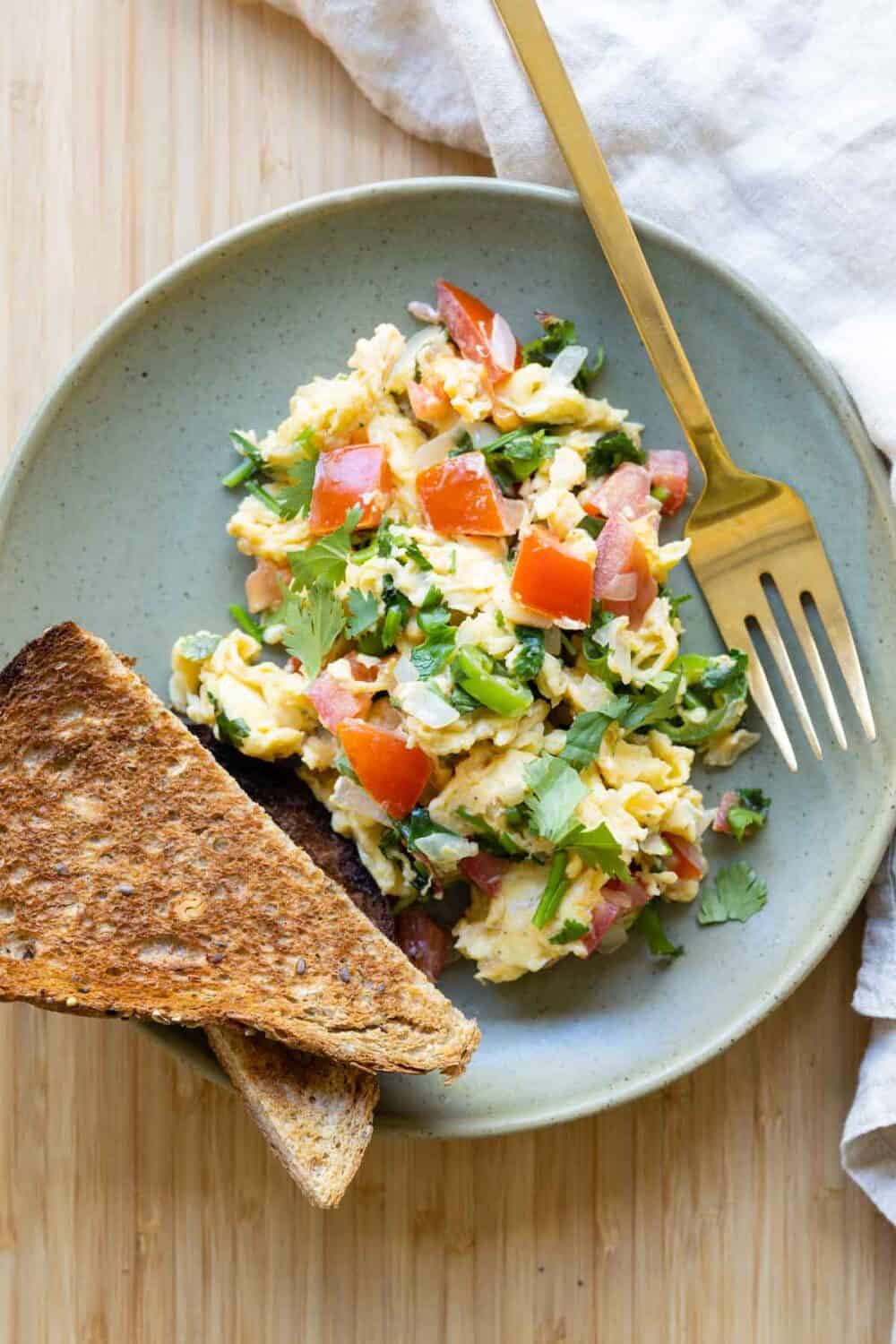 Mexican scrambled eggs and a piece of toast on a green plate.