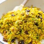 Yellow rice with onions, raisins, peanuts, and parsley in a large white pan.