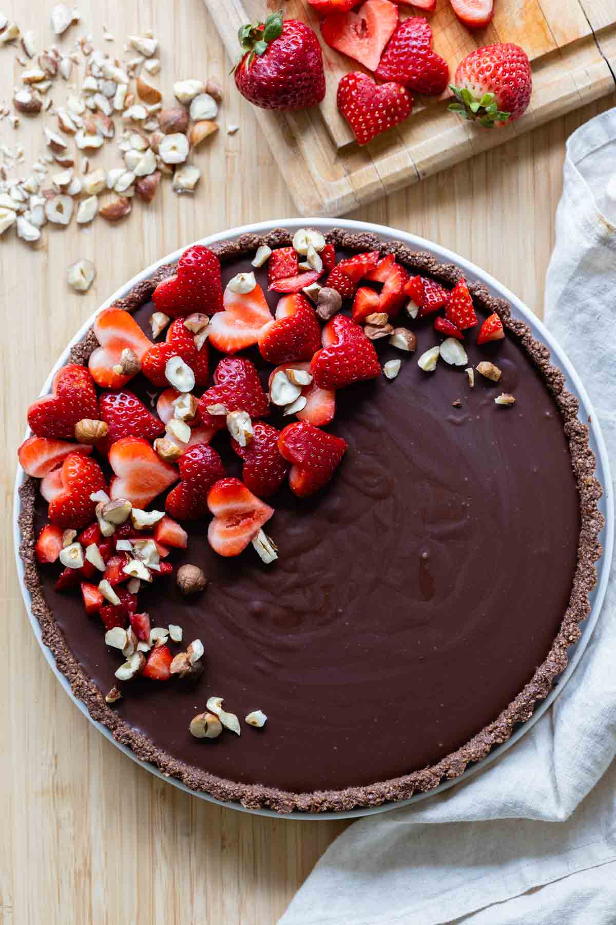 A whole chocolate tart with heart-shaped strawberry pieces on top.